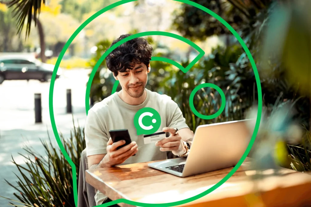 Man outside at a coffee shop paying with his credit card while looking at his phone